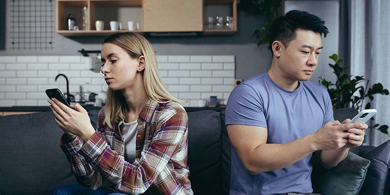 young-multiracial-family-quarreling-sitting-on-the-couch-in-the-room-man-and-woman-on-the-phone-turned-in-different-directions